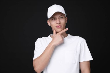 Siyah arka planda şık beyaz beysbol şapkası giyen genç bir adam.