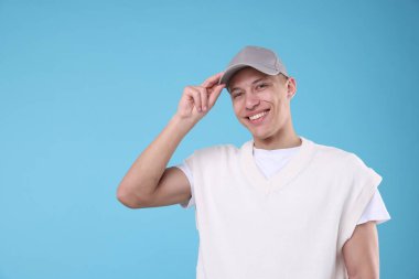 Açık mavi arka planda şık gri beysbol şapkası giyen genç adam, mesaj için yer var.