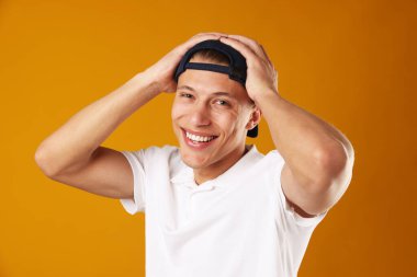 Turuncu arka planda şık beyzbol şapkalı genç adam.