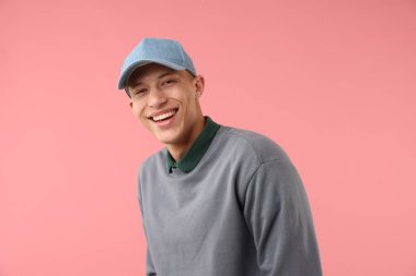 Pembe arka planda şık bir beyzbol şapkası takan genç adam.