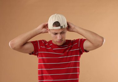 Beyzbol şapkalı genç adam bej arka planda.