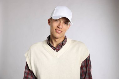 Açık gri arka planda şık bir beyzbol şapkası takan genç adam.