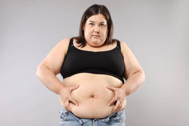 Gri arka planda aşırı göbek yağlı bir kadın. Aşırı kilolu