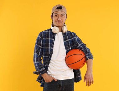 Kulaklıklı ve turuncu arka planda basketbol topu olan bir öğrenci.