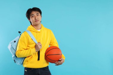 Basketbol topu ve açık mavi arka planda sırt çantası olan öğrenci, metin için boşluk