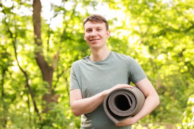 Parkta yoga minderi olan genç bir adam.