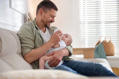 Babam evdeki kanepede bebeğini biberonla besliyor. Metin için boşluk