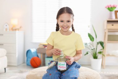 Kız evde cep harçlığını kavanoza koyuyor.