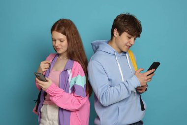 Açık mavi arka planda akıllı telefonları olan genç kız ve oğlan.