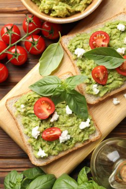 Avokadolu lezzetli sandviçler, domatesler, fesleğen ve peynir ahşap masada, düz uzanmış.