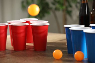 Bira pong oyunu. İçkili plastik bardaklar ve toplar ahşap masada, yakın plan.