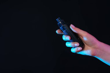 Siyah arka planda neon ışıklı elektronik sigara içen kadın, yakın plan. Metin için boşluk
