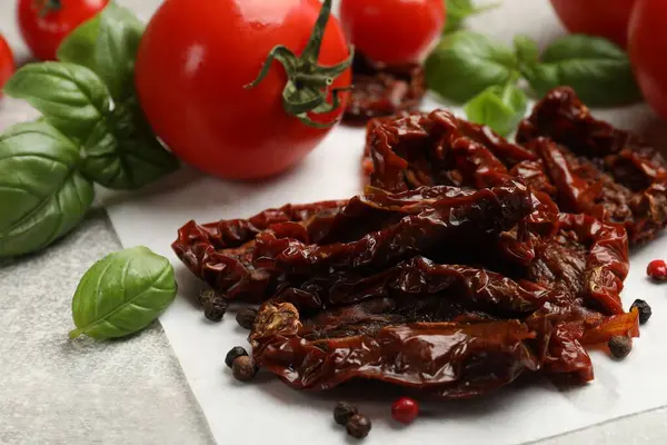 Lezzetli güneşte kurutulmuş domatesler, taze sebzeler ve baharatlar gri desenli masada, yakın plan.