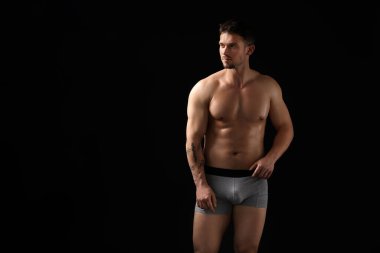 Siyah arka planda açık gri iç çamaşırlı genç bir adam. Metin için boşluk