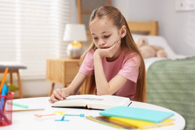 Disleksi. İçerideki masada kitap okuyan üzgün küçük kız.