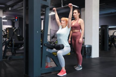 Spor salonunda profesyonel antrenör tarafından yönetilen son sınıf kadın çekme makinesi eğitimi.