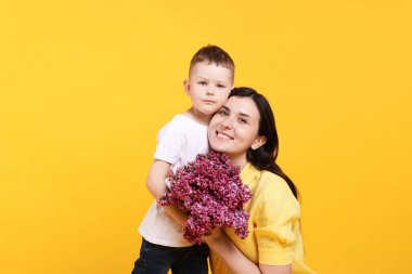 Anne ve oğlu sarı arka planda bir demet leylak çiçeğiyle