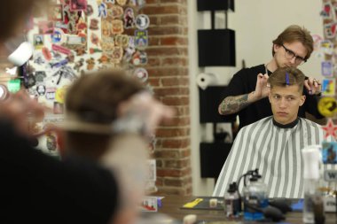 Profesyonel berber, berber dükkanında müşterinin saçını makasla kesiyor.