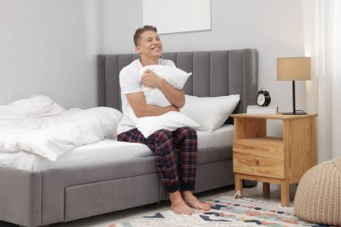 Yastıklı adam evde rahat bir yatakta oturuyor.