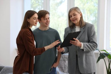 Gülümseyen bir emlakçı pano ile evde çiftlerle çalışıyor.