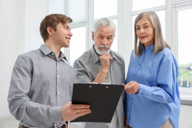 Gülümseyen bir emlakçı pano ile evde çiftlerle çalışıyor.