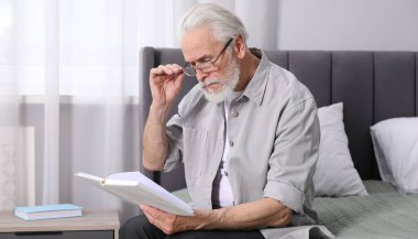 Görme sorunu olan son sınıf öğrencisi evde yatağında kitap okuyor.