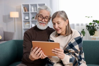 Mutlu yaşlı çift evdeki kanepede tablete bakıyor.