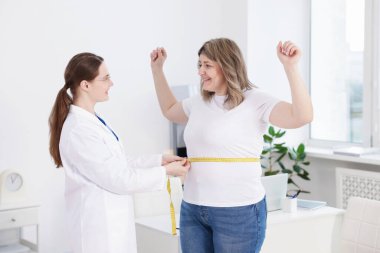 Kilo kaybı. Beslenme uzmanı klinikte kilolu kadının belini bantla ölçüyor.