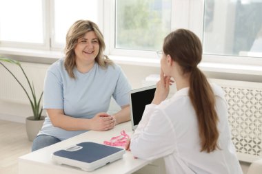 Kilo kaybı. Klinikteki beyaz masada aşırı kilolu kadınlara danışmanlık yapan beslenme uzmanı.