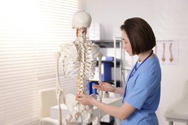 Doktor klinikteki insan iskeleti parçalarına işaret ediyor.