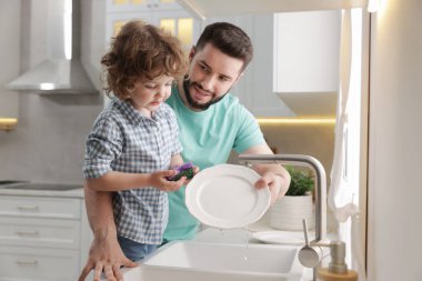 Baba ve oğlu evde birlikte bulaşık yıkıyorlar.