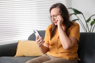 Görme sorunu olan bir kadın evdeki koltukta akıllı telefon kullanıyor, mesaj atmak için yer var.