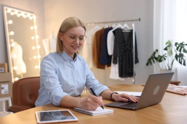 Dükkan sahibi terzisindeki masada dizüstü bilgisayarla çalışırken not alıyor.
