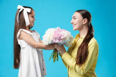 Sevimli küçük kız annesine açık mavi arka planda şakayık demeti veriyor.