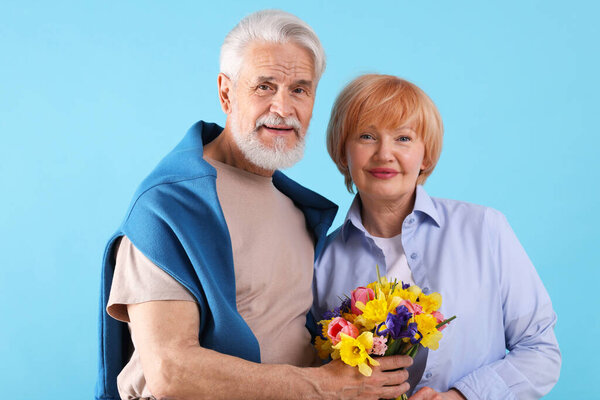 Lovely senior couple with bouquet of flowers on light blue background