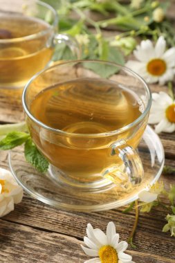 Cam bardaklarda aromatik bitki çayı, ahşap masada nane ve çiçekler, yakın plan.