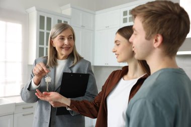 Gülümseyen emlakçı, mutfağın yeni sahibine evinin anahtarını veriyor.