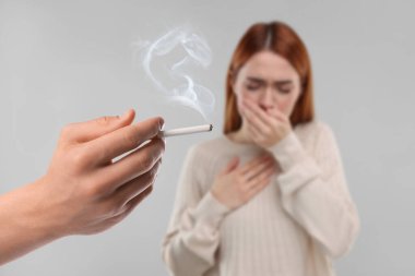 Pasif içicilik. Kadın, açık gri arka planda sigara içen bir adam yüzünden öksürüyor. Seçici odak