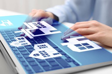 Emlakçı, masadaki dizüstü bilgisayarla ev arıyor. Yakın plan. Aygıt üzerine farklı binaların çizimleri