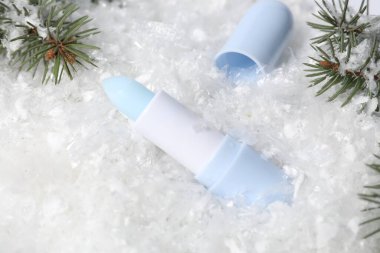 Nemlendirici dudak kremi ve suni kar üzerinde köknar ağacı dalları, yakın plan. Kış bakımı