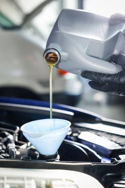 İşçi motor yağını teneke kutudan araba motoruna boşaltıyor.