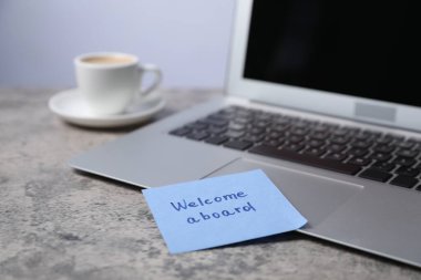 Cümle ile yapışkan not Gemiye hoş geldiniz, laptop ve kahve gri masada, yakın plan