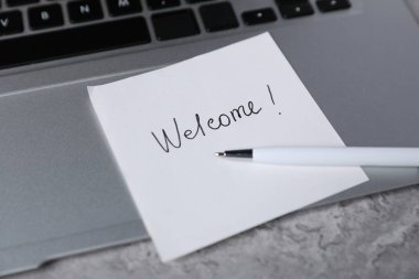 Kelime yapış yapış bir not Hoş geldin, kalem ve dizüstü bilgisayar gri masada, yakın plan