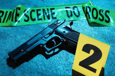 Adli tıp uzmanlığı. Suç mahalli bandı ve silah mavi arka planda, yakın plan. Renkli tonlama efekti