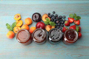 Kavanozlardaki farklı reçeller ve mavi ahşap masa üzerindeki malzemeler.