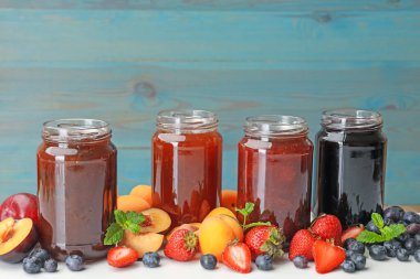 Kavanozlardaki farklı reçeller ve beyaz masadaki malzemeler. Metin için boşluk