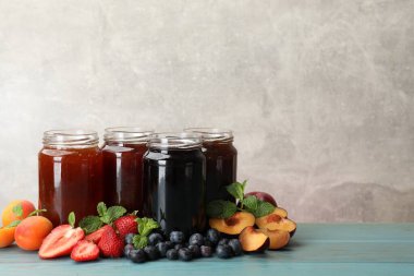 Kavanozlardaki farklı reçeller ve mavi ahşap masadaki malzemeler. Metin için boşluk