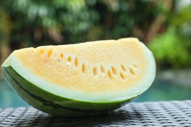 Açık havuz kenarında hasır masada lezzetli bir karpuz dilimi, yakın plan.