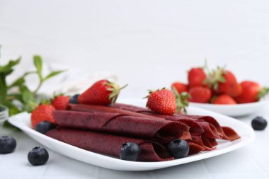 Lezzetli meyve dürümleri, çilekler ve yaban mersinleri beyaz masada, yakın plan. Metin için boşluk