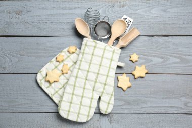 Fırın eldiveninde farklı mutfak aletleri ve açık gri ahşap masada yıldız şeklinde kurabiyeler.